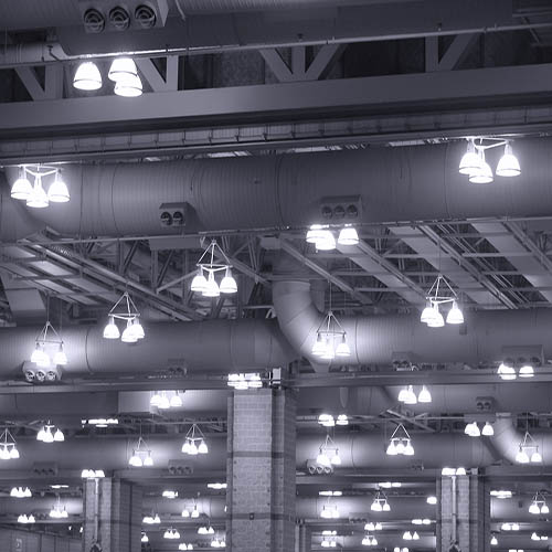 Overhead commercial lights fixtures with mercury vapor discharge lamps hanging from the ceiling of a large industrial building